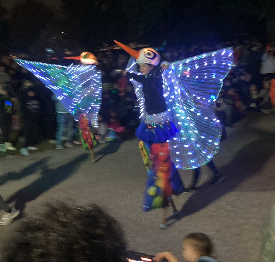 women on stilts with facemasks and LED lights