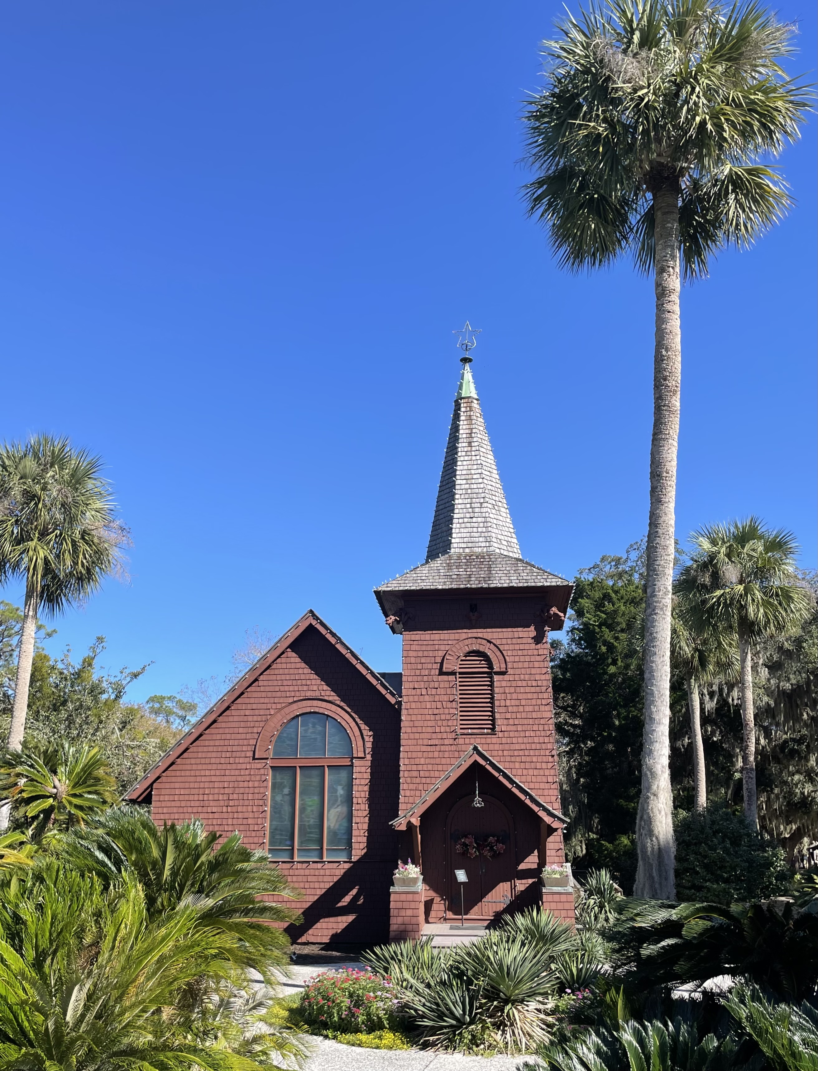 A reddish chapel with steeple and two palm trees