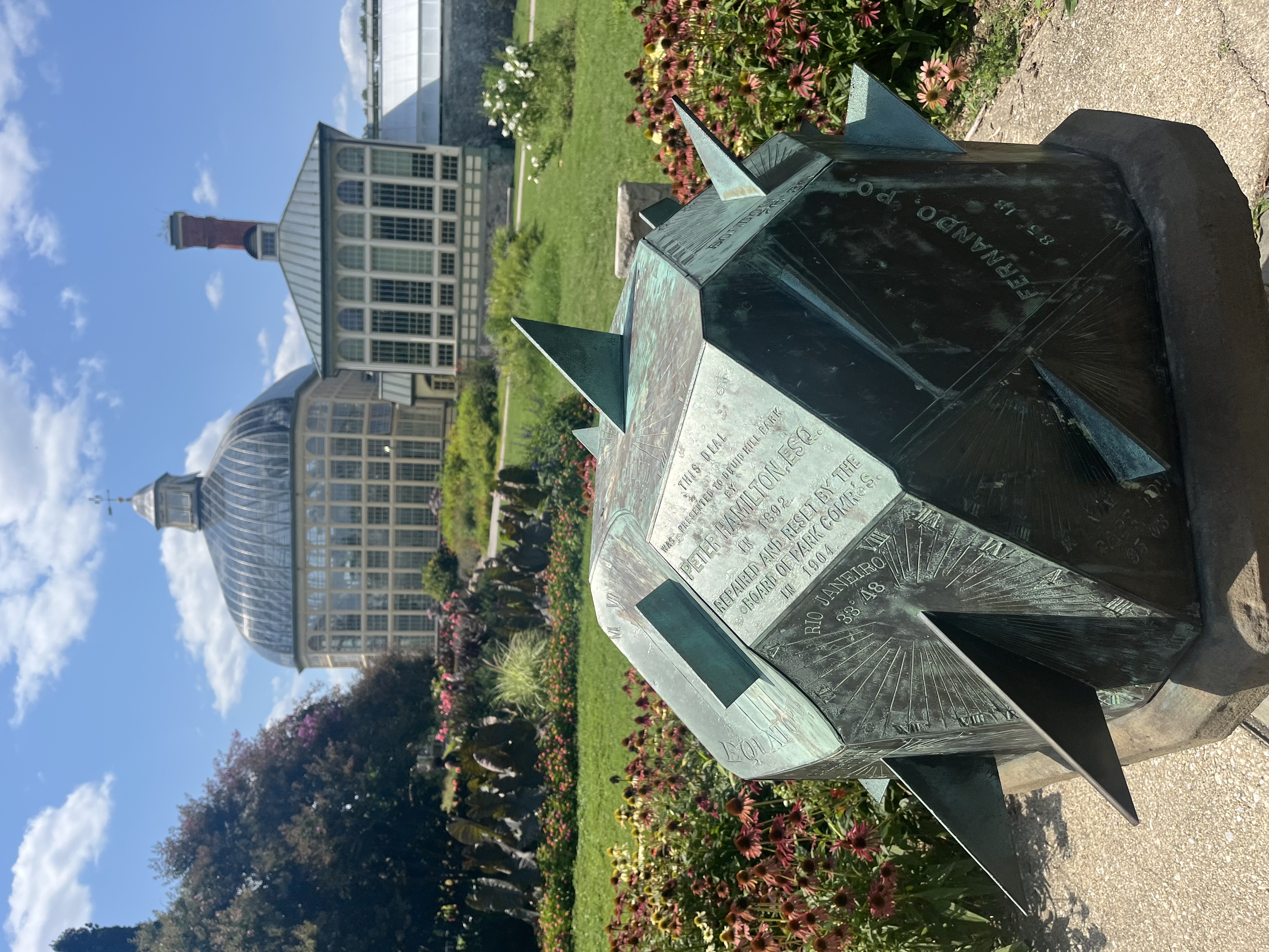 a complex multi-faceted sundial in front of a Victorian greenhouse. 